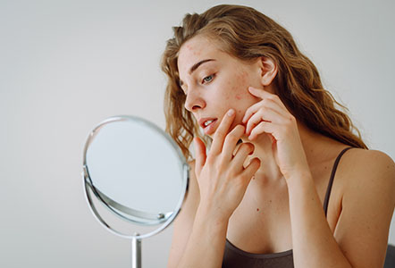 A beautiful woman looking in the mirror, touching her face with her hand, examines acne, pigmentation.